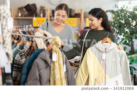 Latin woman with woman companion is busy looking at clothes items, choose winter coat or jacket Latin woman with woman companion is busy looking at clothes items, choose winter coat or jacket 141912069