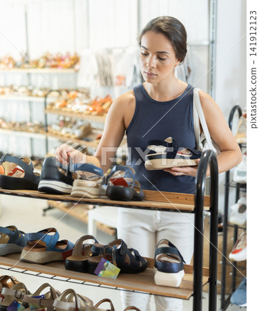Young woman choosing sandals in shoe store Young woman choosing sandals in shoe store 141912123