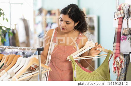 Woman chooses dresses or o tops for the summer period in fashionable clothing store Woman chooses dresses or o tops for the summer period in fashionable clothing store 141912142