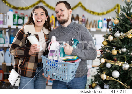 Happy man and woman with full basket choosing presents or something for holidays in household department Happy man and woman with full basket choosing presents or something for holidays in household department 141912161