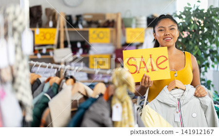 Young woman holding sale sign in clothing store Young woman holding sale sign in clothing store 141912167