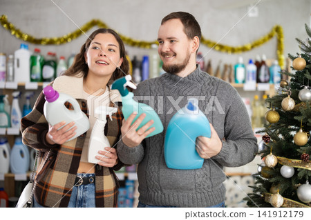 Cheerful married couple customer buying spray and detergent in store decorated for New Year holiday Cheerful married couple customer buying spray and detergent in store decorated for New Year holiday 141912179