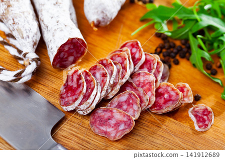 Sliced sausage fuet on cutting board with arugula and black pepper Sliced sausage fuet on cutting board with arugula and black pepper 141912689