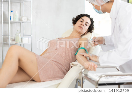 Middle-aged woman having vein injection lying on clinical chair Middle-aged woman having vein injection lying on clinical chair 141912709