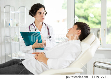 Middle-aged female doctor signing papers while talking with man patient Middle-aged female doctor signing papers while talking with man patient 141912719