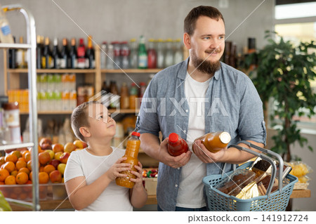 Young man with tween son choosing natural juices in grocery store Young man with tween son choosing natural juices in grocery store 141912724