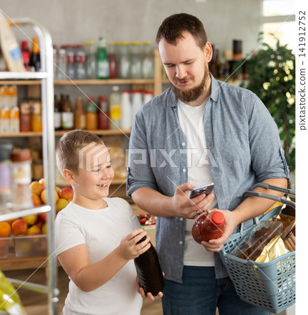 Man with preteen son scanning barcode on juice bottle with phone in store 141912752