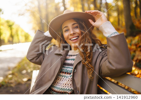Happy woman enjoying autumn weather in the sunny park. Enjoying nature. Fashion, style concept. 141912960