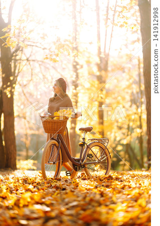Stylish woman with a bicycle enjoying autumn weather in the park. Beautiful Woman in the autumn forest. 141912998