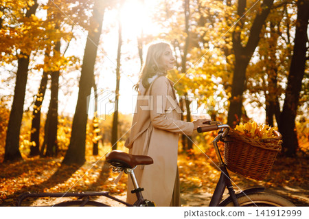 Stylish woman with a bicycle enjoying autumn weather in the park. Beautiful Woman in the autumn forest. Stylish woman with a bicycle enjoying autumn weather in the park. Beautiful Woman in the autumn forest. 141912999
