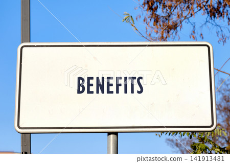 The sign shows the word benefits in large letters. It is located outdoors, surrounded by trees and a clear blue sky The sign shows the word benefits in large letters. It is located outdoors, surrounded by trees and a clear blue sky 141913481