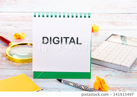 A notebook opened to a page with the word digital is seen on a desk along with a magnifying glass, stationery, and a calculator. The setting is an office A notebook opened to a page with the word digital is seen on a desk along with a magnifying glass, stationery, and a calculator. The setting is an office 141913497