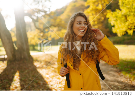 Happy female hiker in yellow coat walking in golden autumn forest. Woman has fun in autumn in park. Happy female hiker in yellow coat walking in golden autumn forest. Woman has fun in autumn in park. 141913813