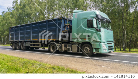 Blue semi-truck with a fully loaded cargo trailer driving along countryside road. Lorry travels. Transport, cargo delivery concept Blue semi-truck with a fully loaded cargo trailer driving along countryside road. Lorry travels. Transport, cargo delivery concept 141914110