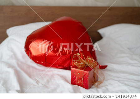 Red heart shaped balloon and gift box on bed Red heart shaped balloon and gift box on bed 141914374