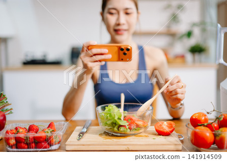 Fitness woman recording healthy smoothie preparation with smartphone in modern kitchen, fresh vegetables and fruit ingredients, healthy lifestyle Fitness woman recording healthy smoothie preparation with smartphone in modern kitchen, fresh vegetables and fruit ingredients, healthy lifestyle 141914509