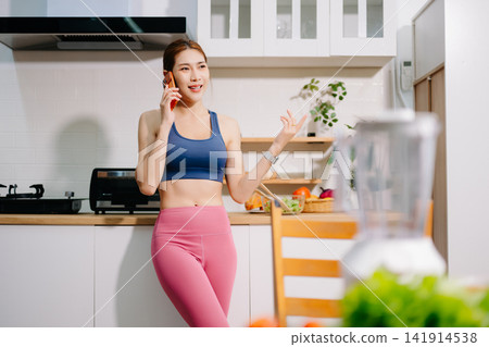 Fitness woman reading recipe while preparing healthy smoothie with fresh vegetables in modern kitchen. Healthy lifestyle, nutrition, home cooking Fitness woman reading recipe while preparing healthy smoothie with fresh vegetables in modern kitchen. Healthy lifestyle, nutrition, home cooking 141914538