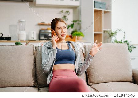 Young woman using smartphone with headphones at home, digital lifestyle, social media, music streaming, mobile app usage in modern living space. Young woman using smartphone with headphones at home, digital lifestyle, social media, music streaming, mobile app usage in modern living space. 141914540