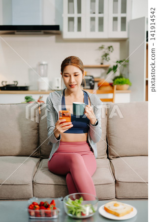 Young woman enjoying healthy meal at home after workout, clean eating lifestyle concept, fitness diet, wellness routine in cozy modern living space. 141914542