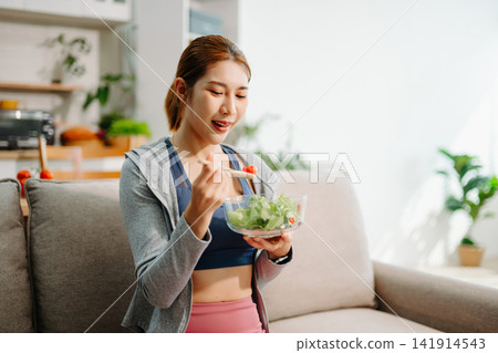 Young woman enjoying healthy meal at home after workout, clean eating lifestyle concept, fitness diet, wellness routine in cozy modern living space. Young woman enjoying healthy meal at home after workout, clean eating lifestyle concept, fitness diet, wellness routine in cozy modern living space. 141914543