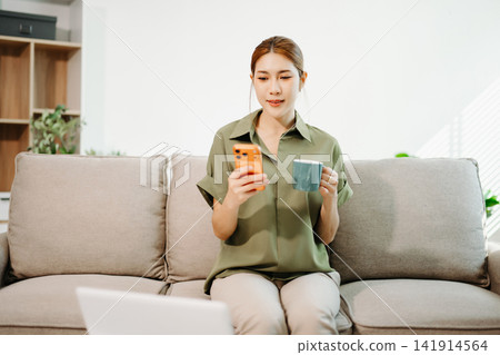 Focused financial management. Smiling Asian woman reviewing paperwork and using a laptop for budget planning and remote work Focused financial management. Smiling Asian woman reviewing paperwork and using a laptop for budget planning and remote work 141914564