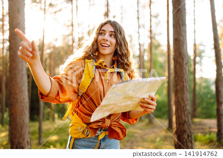 A traveler woman stands in a lush forest, examining a map with a focused expression 141914762