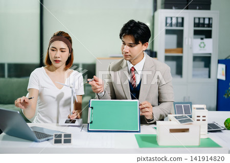 Business professionals using solar and wind models to plan sustainable green energy and ESG initiatives in a modern corporate office. Business professionals using solar and wind models to plan sustainable green energy and ESG initiatives in a modern corporate office. 141914820