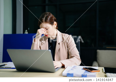 Asian woman feeling migraine head strain.Overworked businesswoman financier while working on laptop and tablet at office. Asian woman feeling migraine head strain.Overworked businesswoman financier while working on laptop and tablet at office. 141914847