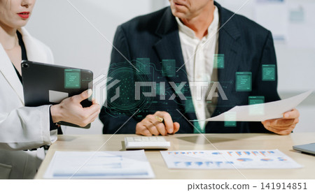 Business professionals using a tablet and digital HUD interface to review structured network data, charts, and corporate information. 141914851