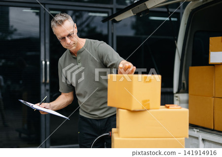 Warehouse worker inspecting parcels with clipboard before loading delivery van. Logistics, inventory, ecommerce shipping, supply chain, fulfillment a Warehouse worker inspecting parcels with clipboard before loading delivery van. Logistics, inventory, ecommerce shipping, supply chain, fulfillment a 141914916