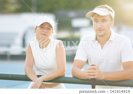 Couple resting after playing tennis on court Couple resting after playing tennis on court 141914919