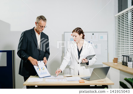 Businessman and corporate businesswoman analyzing financial charts on desk. Professional team collaboration and strategic planning. Businessman and corporate businesswoman analyzing financial charts on desk. Professional team collaboration and strategic planning. 141915043