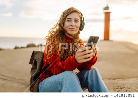 Relaxed woman enjoying music by the waterfront while wearing headphone. Travel and blogging concept Relaxed woman enjoying music by the waterfront while wearing headphone. Travel and blogging concept 141915091