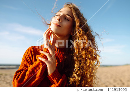 Young woman with curly hair enjoys the sunny beach, smiling and basking in the warmth of clear day Young woman with curly hair enjoys the sunny beach, smiling and basking in the warmth of clear day 141915093