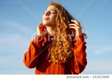 Young woman with curly hair enjoys the sunny beach, smiling and basking in the warmth of clear day Young woman with curly hair enjoys the sunny beach, smiling and basking in the warmth of clear day 141915094
