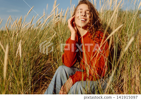 Beautiful young woman enjoying nature outdoors in tall grass. Flying hairs. Lifestyle. Fashion style Beautiful young woman enjoying nature outdoors in tall grass. Flying hairs. Lifestyle. Fashion style 141915097