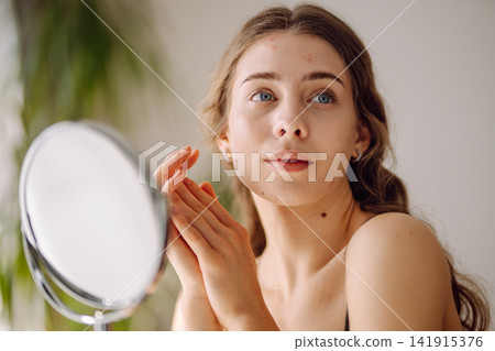 Young woman with problem skin looking into mirror. Inflammation on face, problem skin. Beauty care. Young woman with problem skin looking into mirror. Inflammation on face, problem skin. Beauty care. 141915376