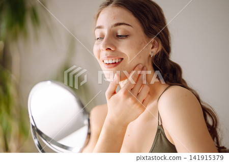 Young woman with problem skin looking into mirror. Inflammation on face, problem skin. Beauty care. Young woman with problem skin looking into mirror. Inflammation on face, problem skin. Beauty care. 141915379