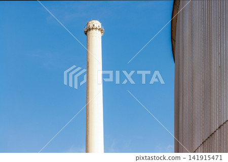 Minimal industrial smokestack and ribbed silo against blue sky. Copy space Minimal industrial smokestack and ribbed silo against blue sky. Copy space 141915471