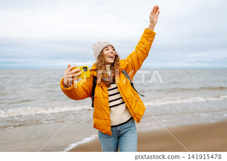Portrait of young tourist in yellow jacket with phone in hands on seashore. Travel concept, blogging 141915478
