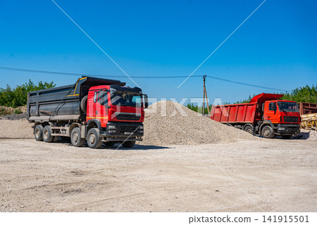 dump trucks are loading gravel at a construction site, viewed from the side, in an industrial setting with a clean background, offering ample copy space for modern design resources. dump trucks are loading gravel at a construction site, viewed from the side, in an industrial setting with a clean background, offering ample copy space for modern design resources. 141915501
