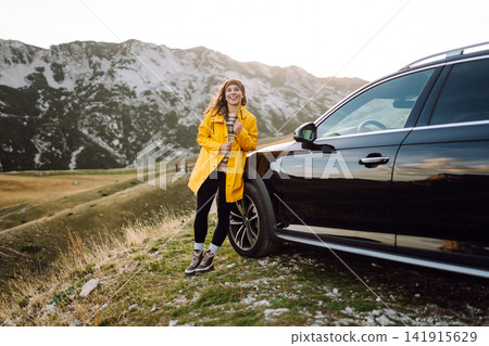A cheerful traveler enjoying a scenic mountain view while sitting on the trunk. Travelling by car. A cheerful traveler enjoying a scenic mountain view while sitting on the trunk. Travelling by car. 141915629