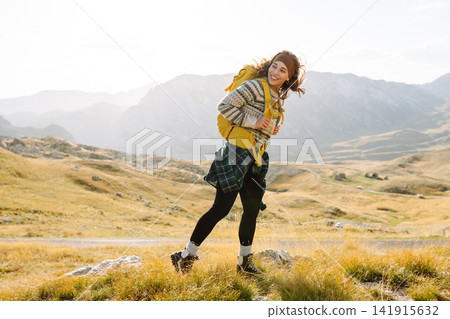 Traveler woman with a bright yellow backpack strolls through golden meadows. Active lifestyle Traveler woman with a bright yellow backpack strolls through golden meadows. Active lifestyle 141915632