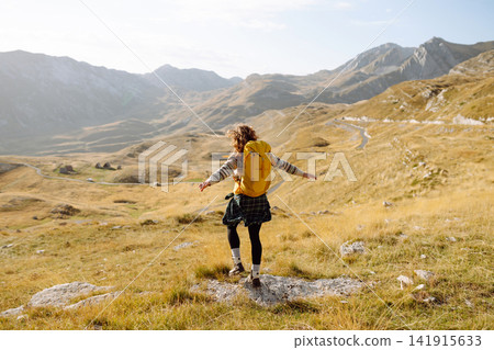 Traveler woman with a bright yellow backpack strolls through golden meadows. Active lifestyle Traveler woman with a bright yellow backpack strolls through golden meadows. Active lifestyle 141915633