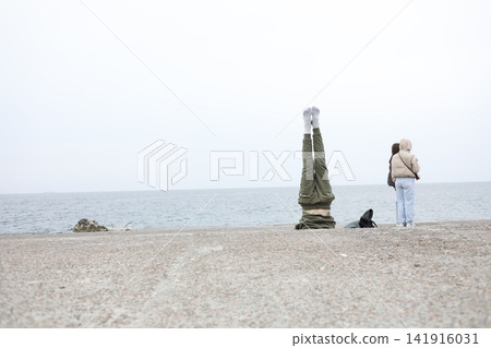 Distant woman walking beside a seaside monument on a quiet beach, with calm water and pale sky creating a minimalist coastal scene of solitude, travel and peaceful reflection time Distant woman walking beside a seaside monument on a quiet beach, with calm water and pale sky creating a minimalist coastal scene of solitude, travel and peaceful reflection time 141916031