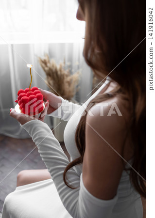 Woman in a white dress sitting by a bright window while holding a red rose, creating a soft romantic lifestyle scene with natural light, elegant mood and peaceful home atmosphere Woman in a white dress sitting by a bright window while holding a red rose, creating a soft romantic lifestyle scene with natural light, elegant mood and peaceful home atmosphere 141916042