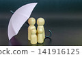 Light pink umbrella shielding wooden figures as a concept of leadership, risk management and security protection 141916125