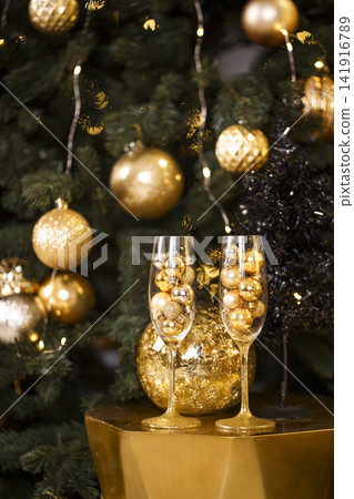 Festive Champagne Glasses Filled with Golden Ornaments by Christmas Tree Festive Champagne Glasses Filled with Golden Ornaments by Christmas Tree 141916789