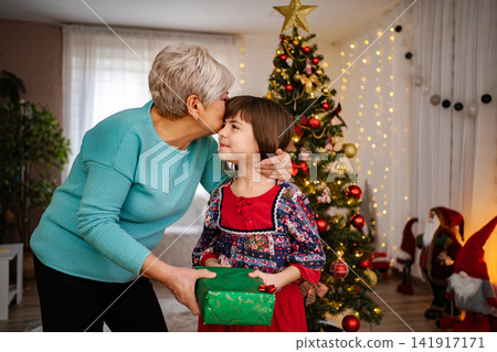 Grandmother kissing child while giving Christmas present Grandmother kissing child while giving Christmas present 141917171