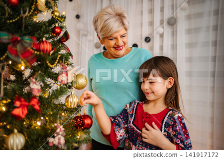 Grandmother and child decorating Christmas tree for holiday celebration 141917172